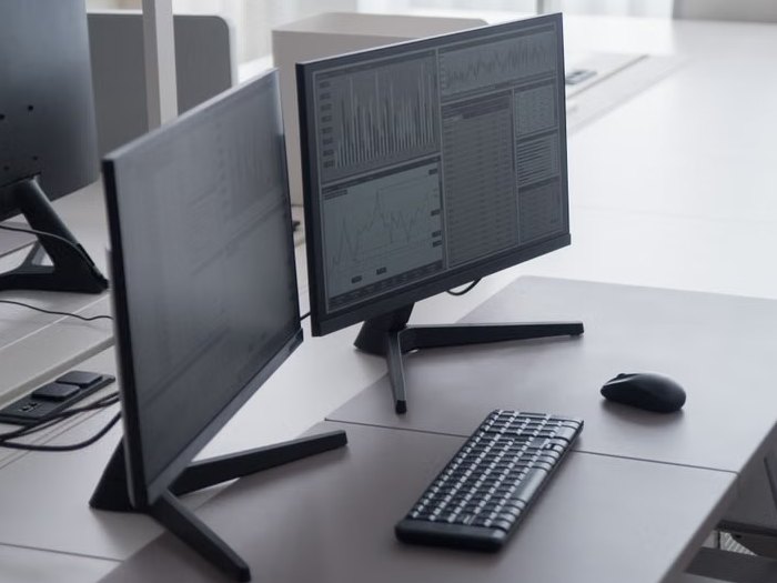Two computer monitors, a keyboard and a mouse on a desk in a bright office