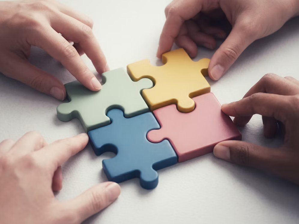 Four pairs of hands fitting colourful puzzle pieces together